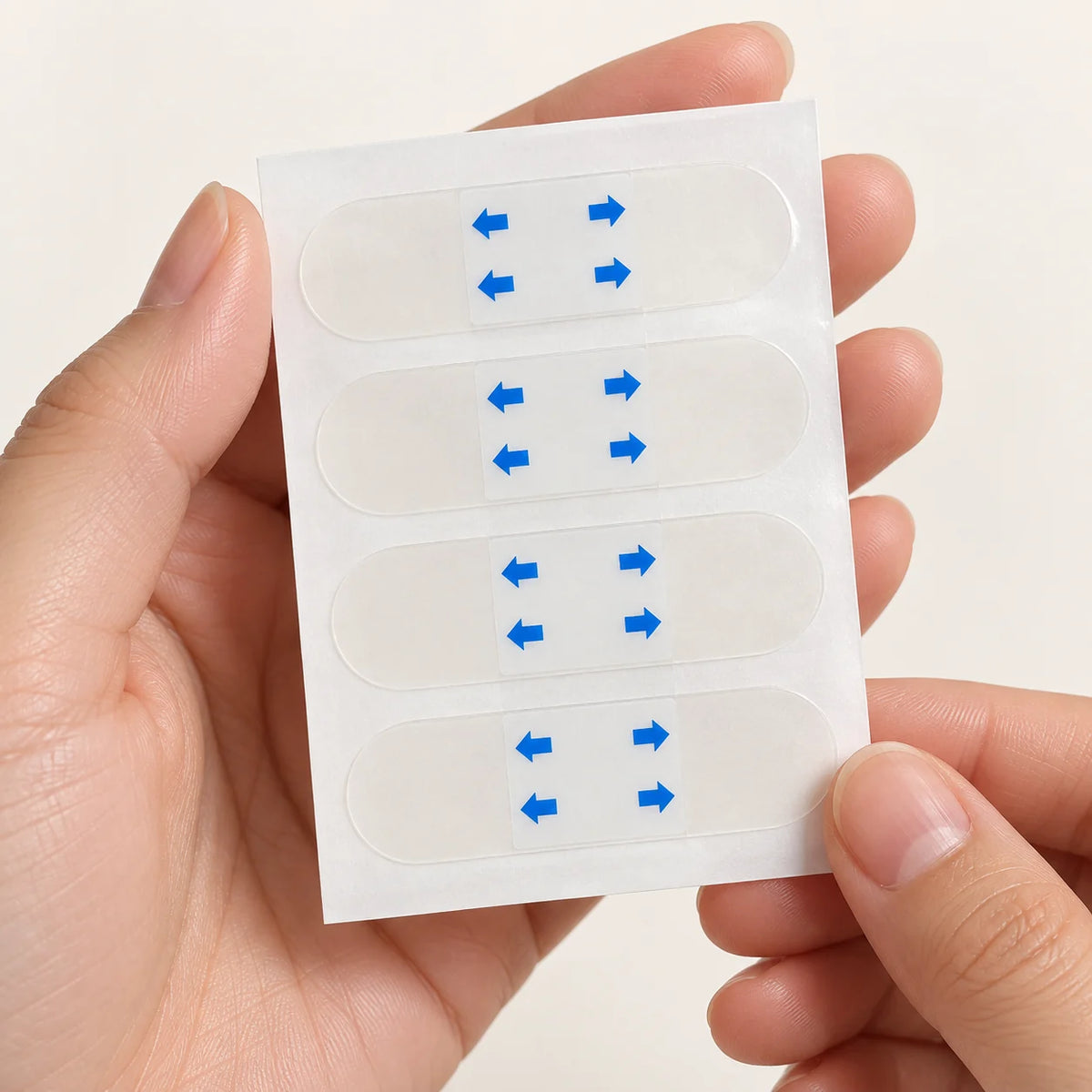 Hands holding a sheet of clear face-lifting strips with four horizontal rows.